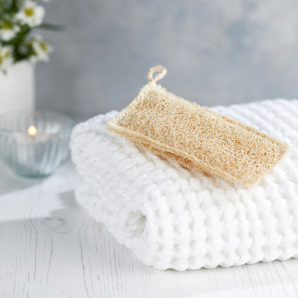 Eco Living reusable loofah scrub pad on a white towel in front of a grey wall