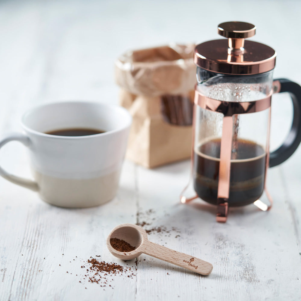 Eco living wooden coffee measure spoon on a grey wooden table next to a white mug of coffee