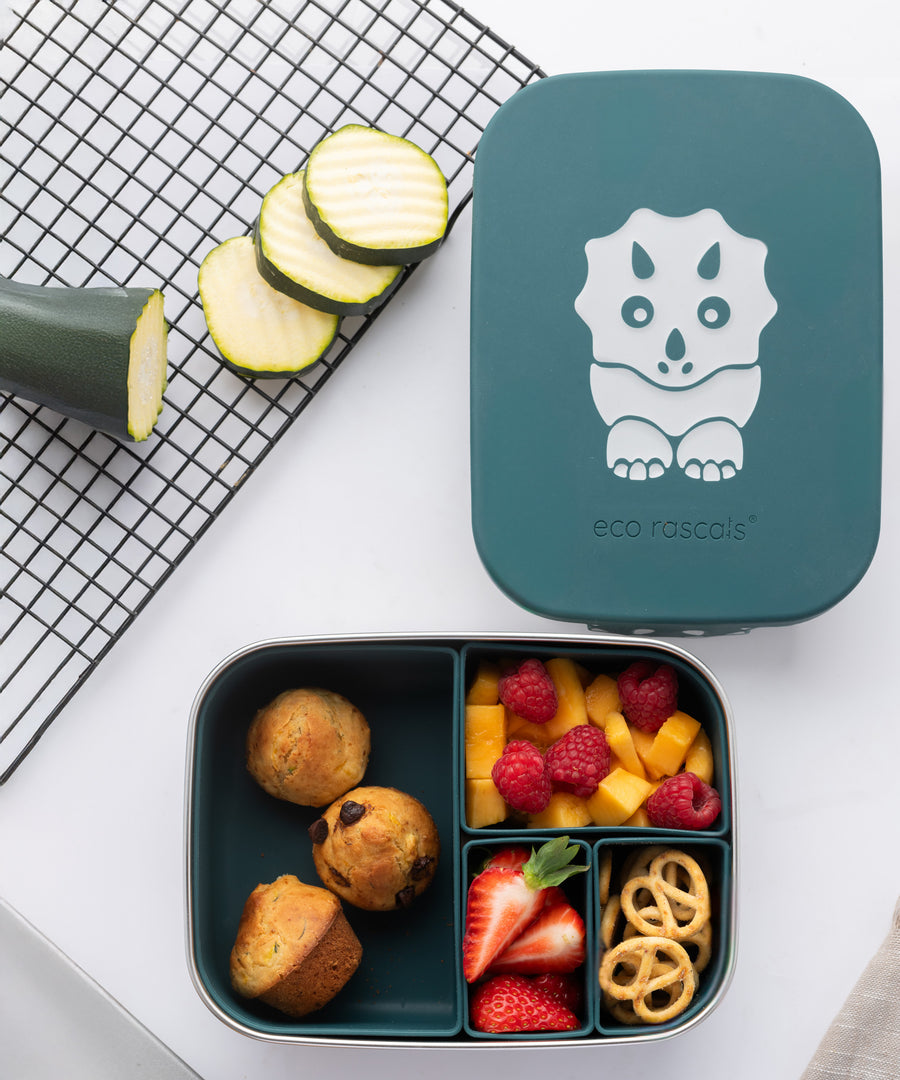 An overhead view of the teal dinosaur design Eco Rascals Stainless Steel Character Lunch Box. Hidden veg muffins are placed in the largest silicone segment, with fruit and pretzels in the other 3 smaller sections. 