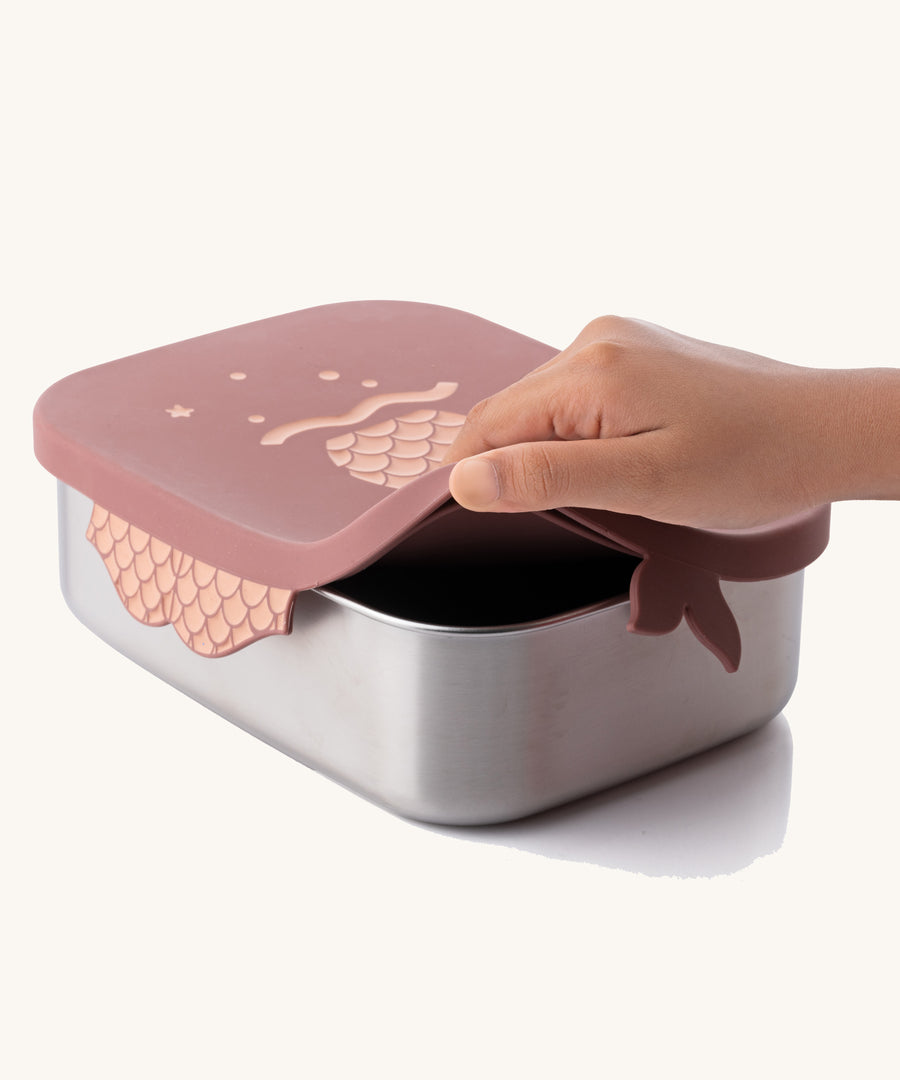 An adult's hand lifting the lid from the rose pink mermaid design Eco Rascals Stainless Steel Character Lunch Box. 