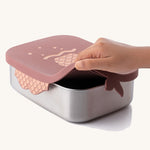 An adult's hand lifting the lid from the rose pink mermaid design Eco Rascals Stainless Steel Character Lunch Box. 