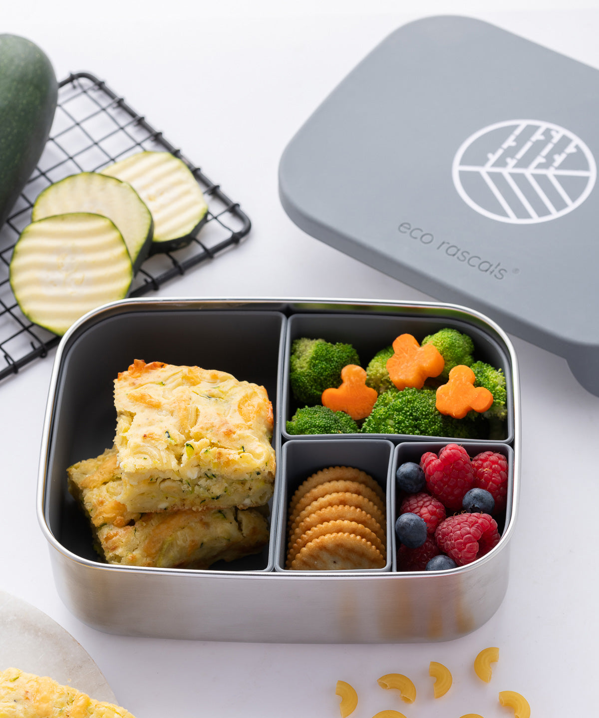 The Eco Rascals Stainless Steel Lunch Box with a silver grey silicone lid and pot inserts. The lid has been taken off and food can be seen in the lunchbox. 