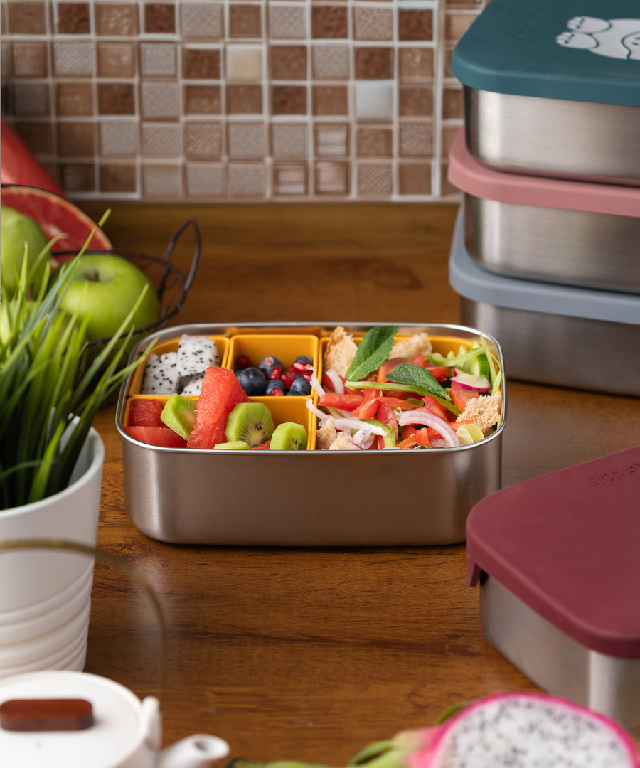 A Eco Rascals Stainless Steel Lunch Box without a lid showing the food inside in the yellow silicone coloured, removable compartment pots. 