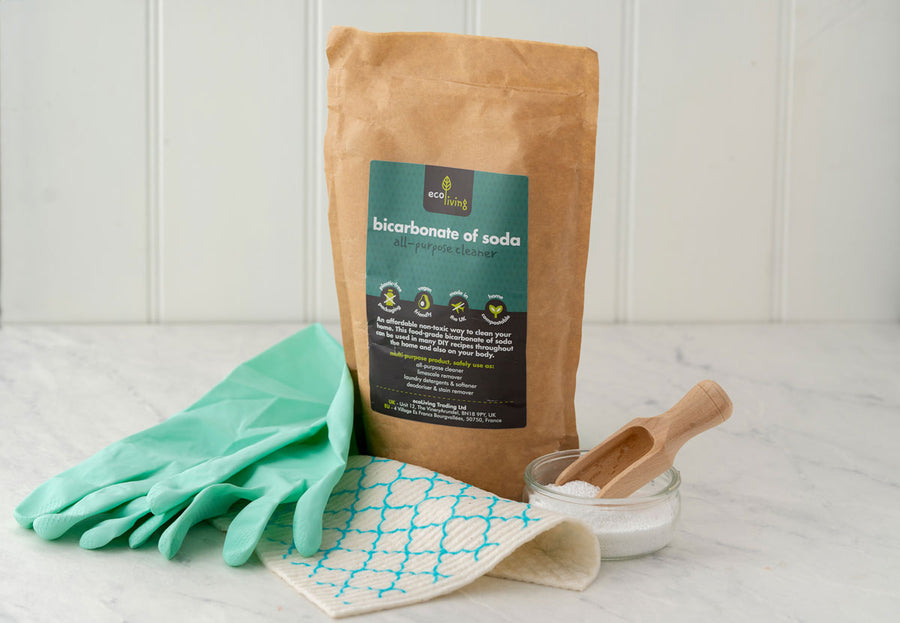 Ecoliving Bicarbonate Of Soda pictured next to green rubber gloves and a wooden scoop placed in a glass tub