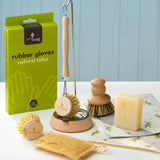 Eco Living cleaning starter contents on a table including the Eco Living natural latex rubber gloves, a wooden dish brush on a dish brush holder, a wooden pot brush, lavender soap and loofah sponge.