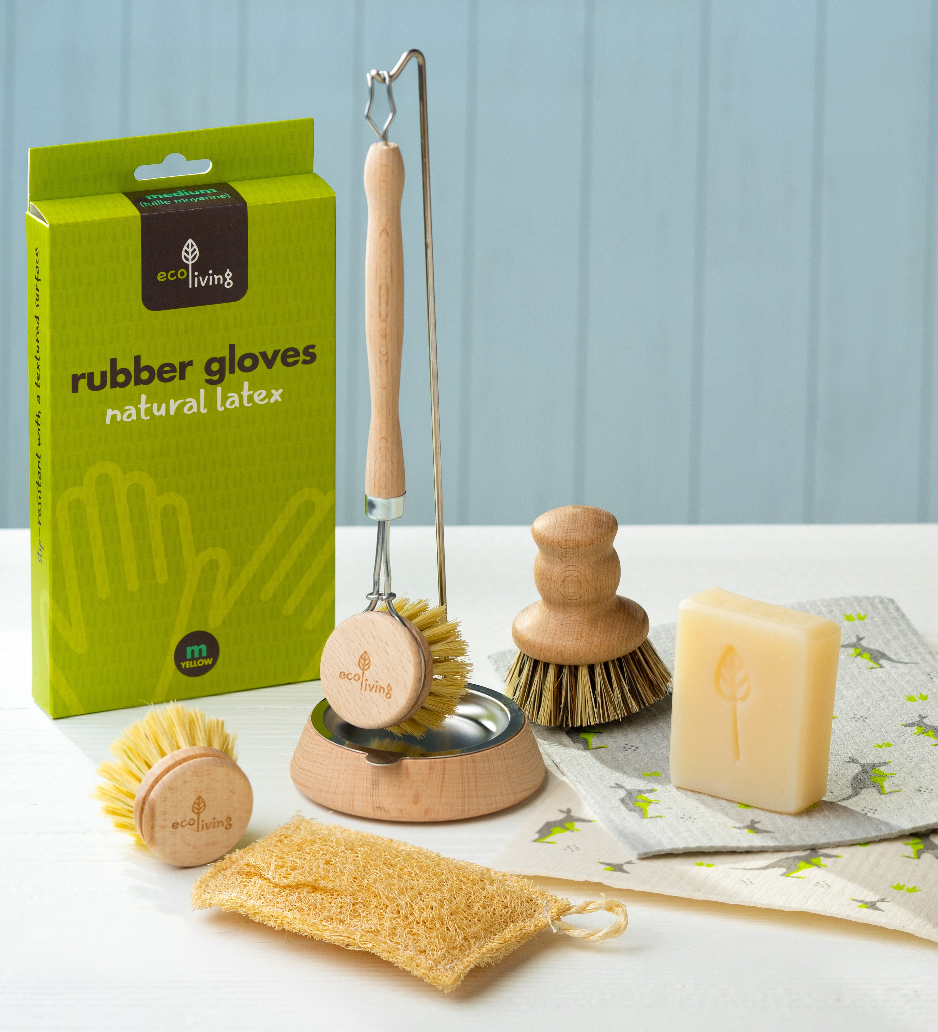 Eco Living cleaning starter contents on a table including the Eco Living natural latex rubber gloves, a wooden dish brush on a dish brush holder, a wooden pot brush, lavender soap and loofah sponge.