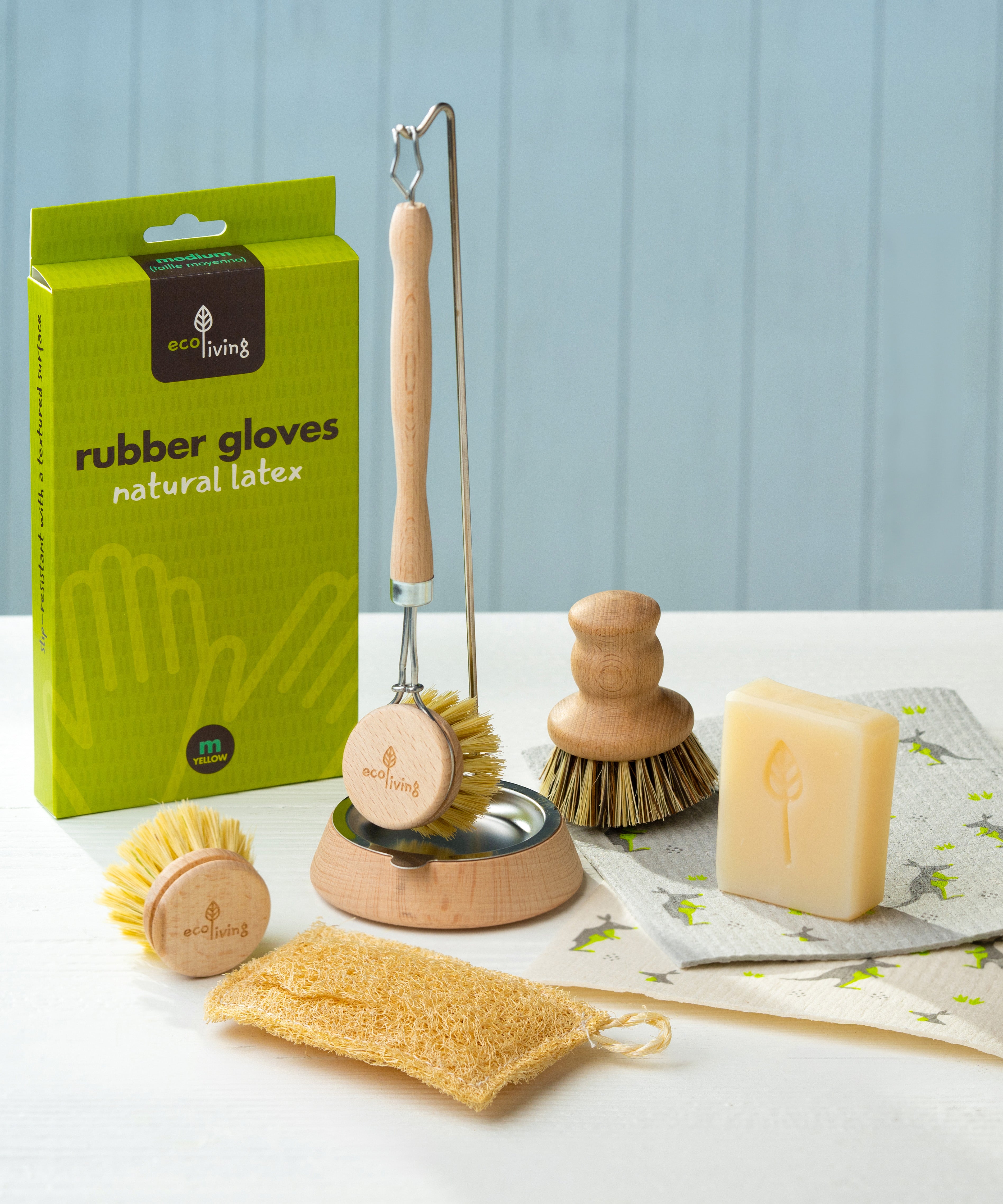 Eco Living cleaning starter contents on a table including the Eco Living natural latex rubber gloves, a wooden dish brush on a dish brush holder, a wooden pot brush, lavender soap and loofah sponge.