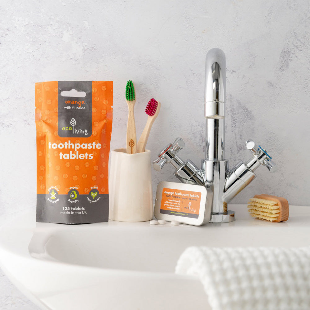 Ecoliving orange flavour toothpaste tablets tin leaning against a silver tap