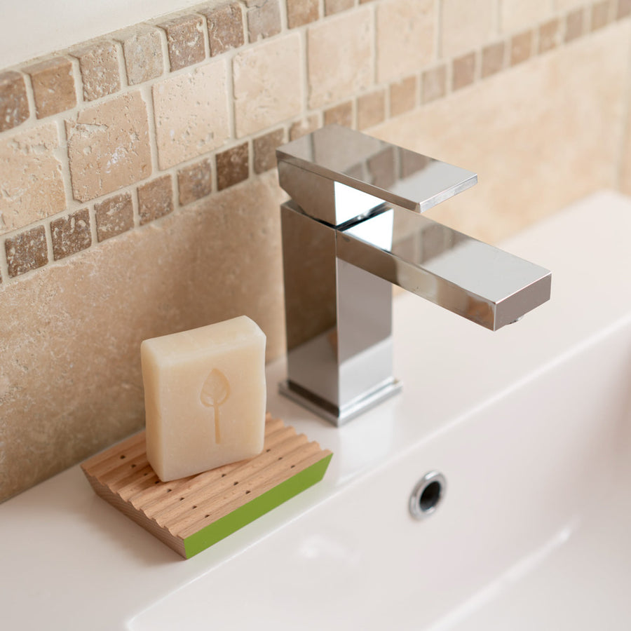 Ecoliving plastic free wooden soap dish with an ecoliving soap on top on a white sink next to a metal tap