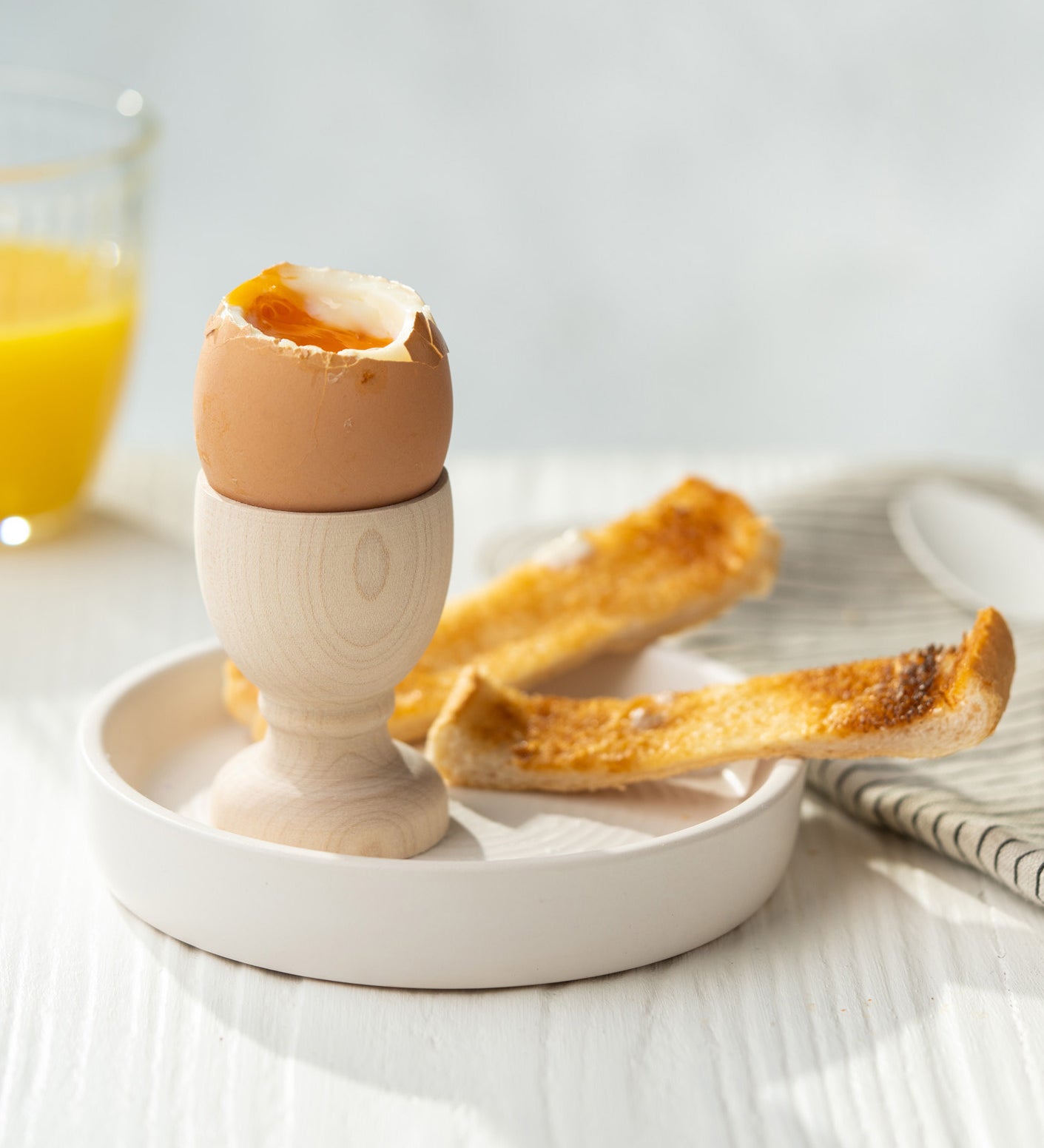 Eco Living wooden egg cup on a dish with an egg on top and 2 small slices of toast 