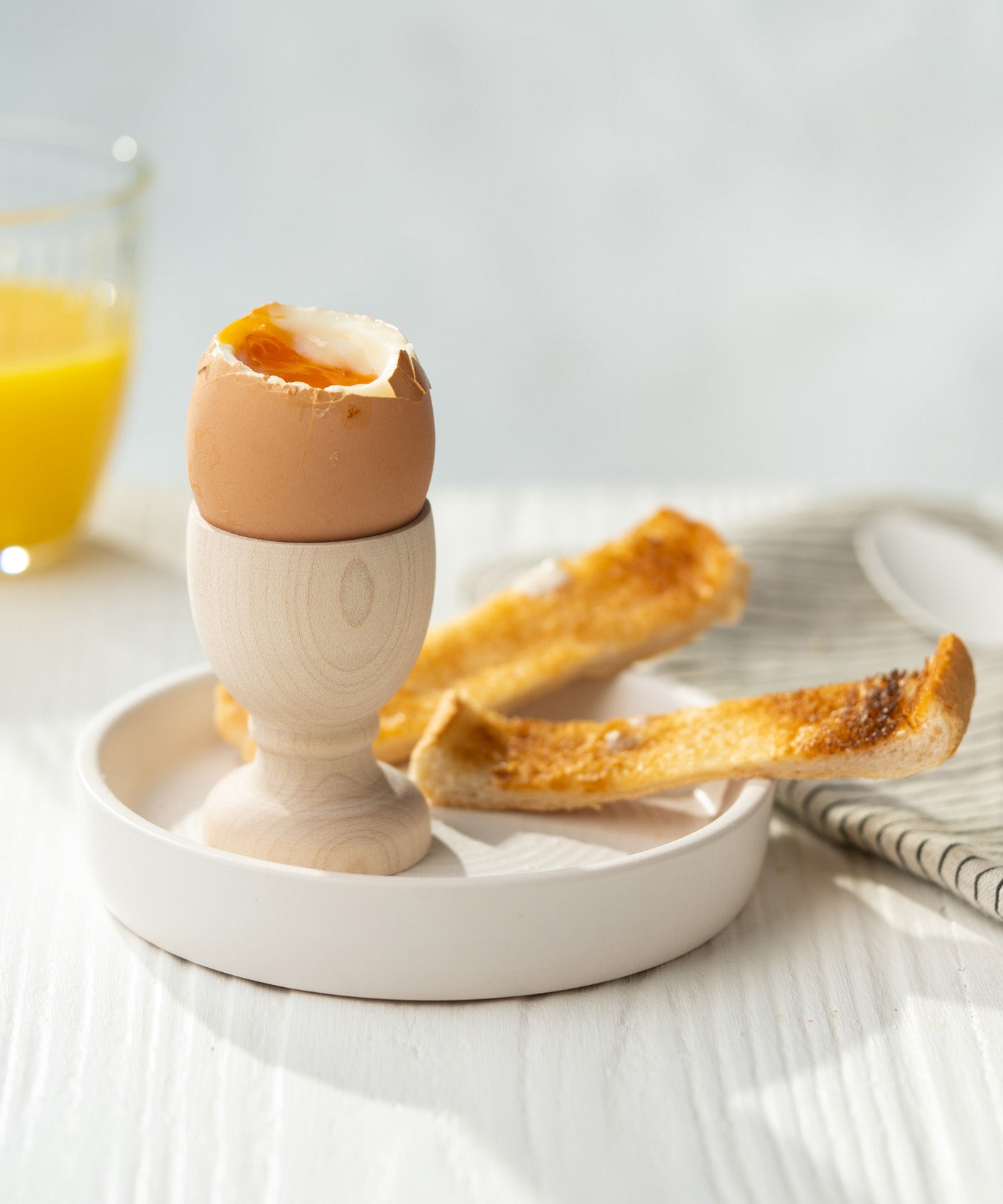 Eco Living wooden egg cup on a dish with an egg on top and 2 small slices of toast 