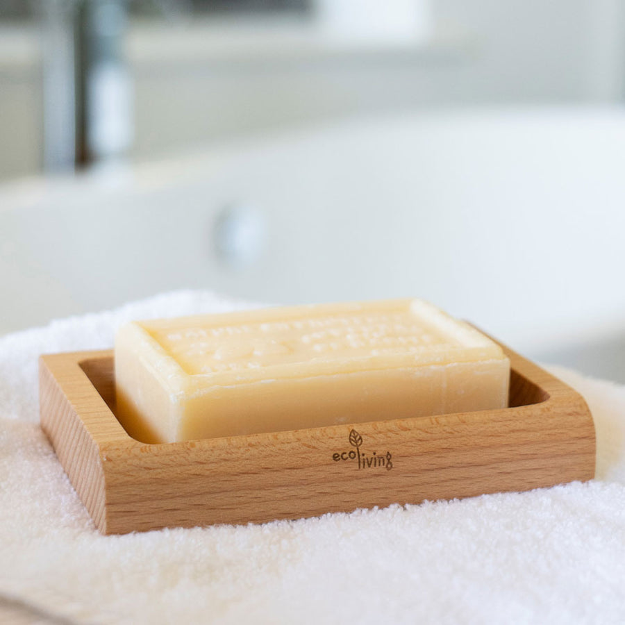 Close up of an Ecoliving plastic-free beech wood soap dish on top of a white towel with a natural soap block inside