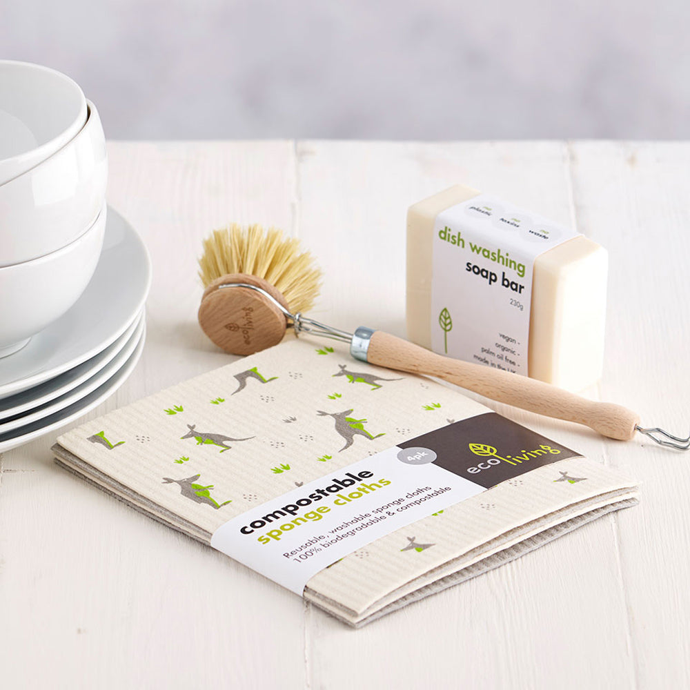 Ecoliving compostable home cleaning cloths laid out on a white table next to a stack of white bowls and kitchenware