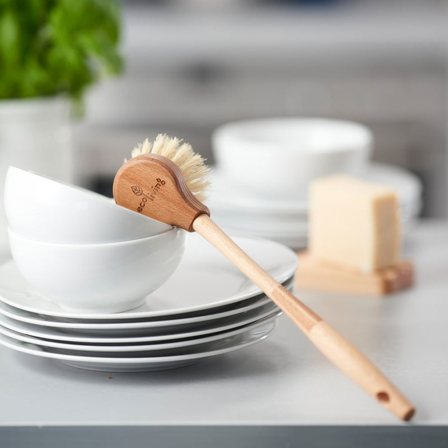 Ecoliving Long Handle Wooden Dish Brush pictured on a stack of white ceramic bowls and plates