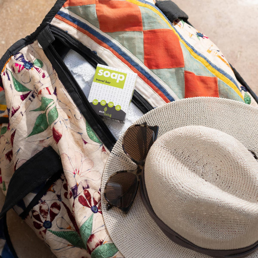 Ecoliving solid travel soap bar on top of an unzipped duffel bag next to a sun hat and sunglasses