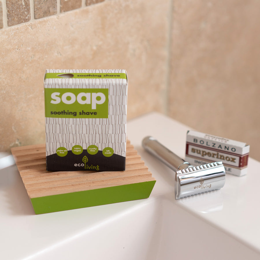 Ecoliving solid shaving soap bar on a wooden soap dish next to a reusable metal razor