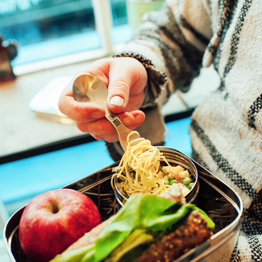 A close up of an adult using the Elepahnt Box Spork to eat noodles from a reusable stainless steel food container