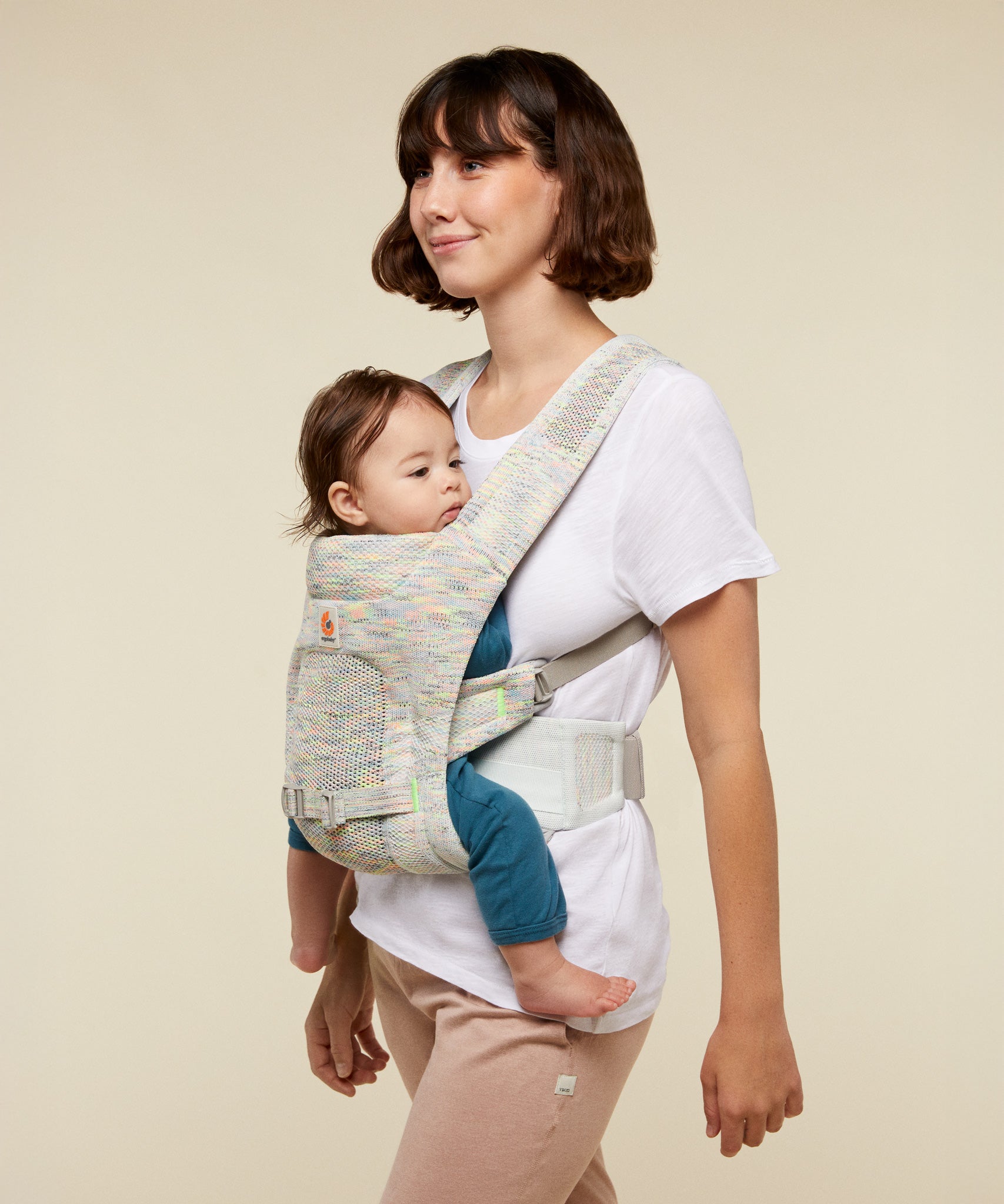 A woman babywearing a young baby using the ErgoBaby Aerloom abalone Baby Carrier.