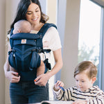 A woman babywearing her baby using a midnigh blue coloured Ergobaby Omni 360 Cool Air Mesh Baby Carrier