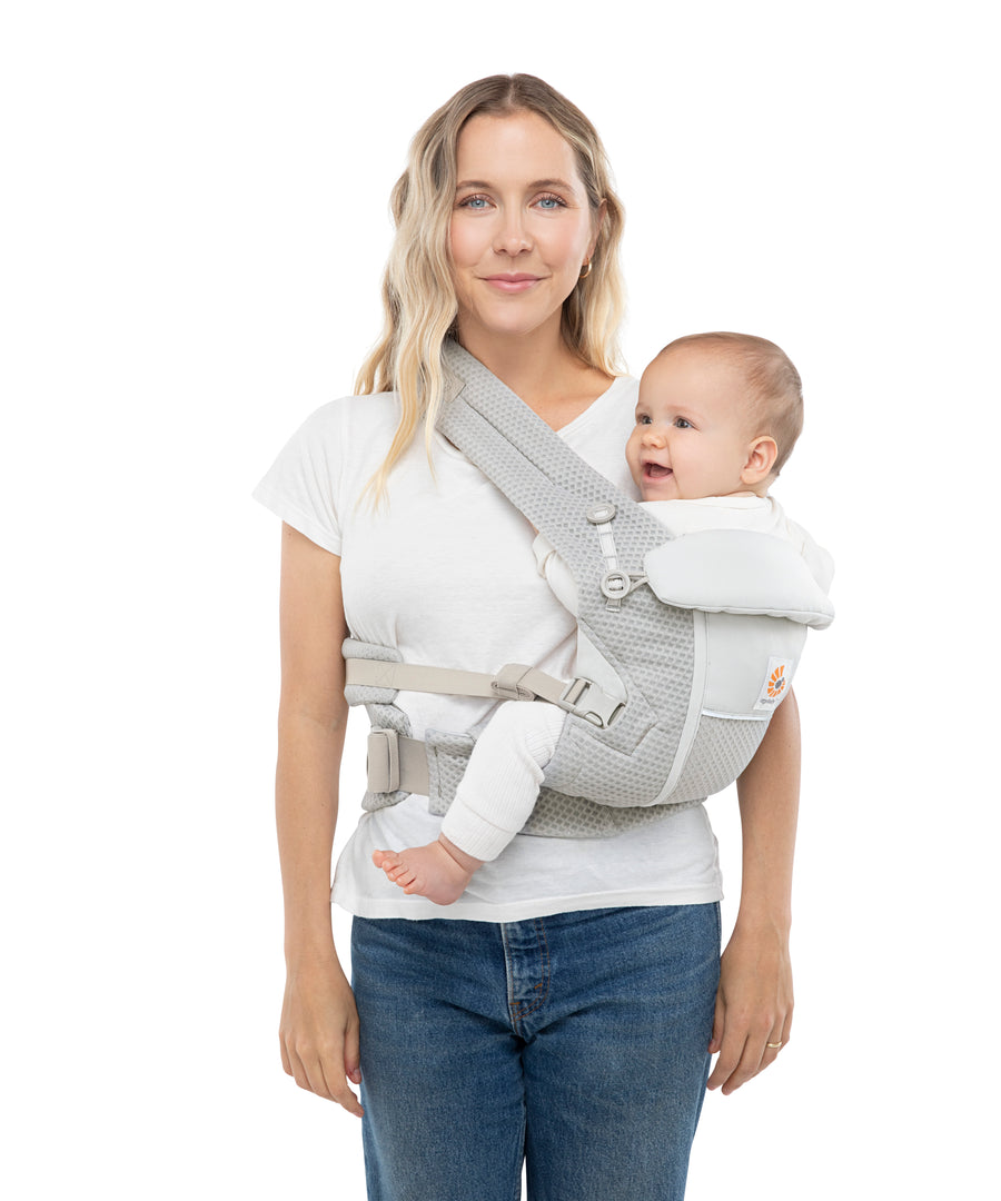 Woman with wavy blonde hair and a white t-shirt wearing her baby on her hip in the Ergobaby Adapt  SoftFlex™ Mesh Baby Carrier in Pearl Grey. Front view, white background. 