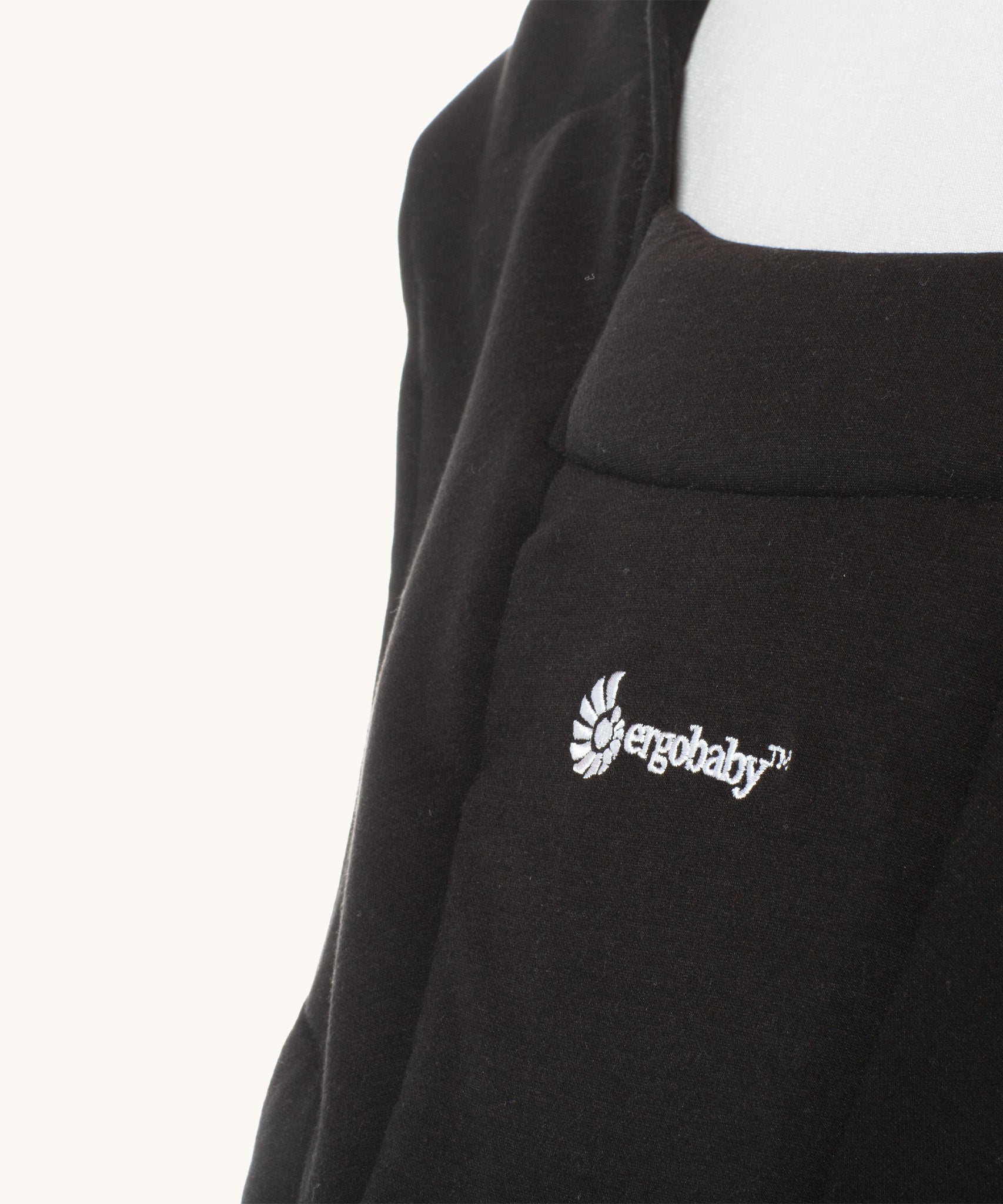 Close up of the Ergobaby logo on the Ergobaby Embrace Soft Knit Newborn Baby Carrier in Pure Black. Side view on a mannequin.