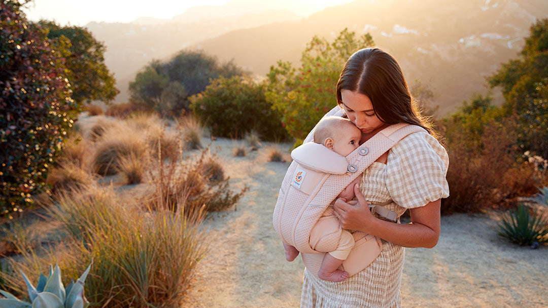 A woman carrying her baby in a pink Ergobaby carrier