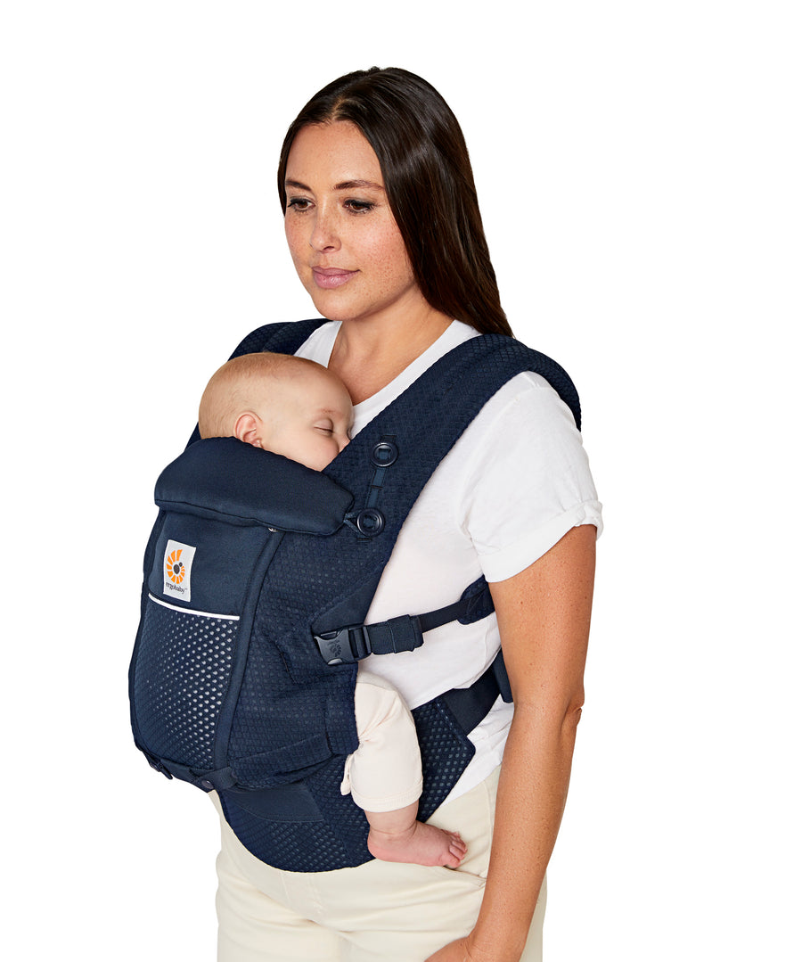 Woman with straight brown hair and a white t-shirt wearing her baby in the Ergobaby Adapt  SoftFlex™ Mesh Baby Carrier in Midnight Blue. Front view, white background. 