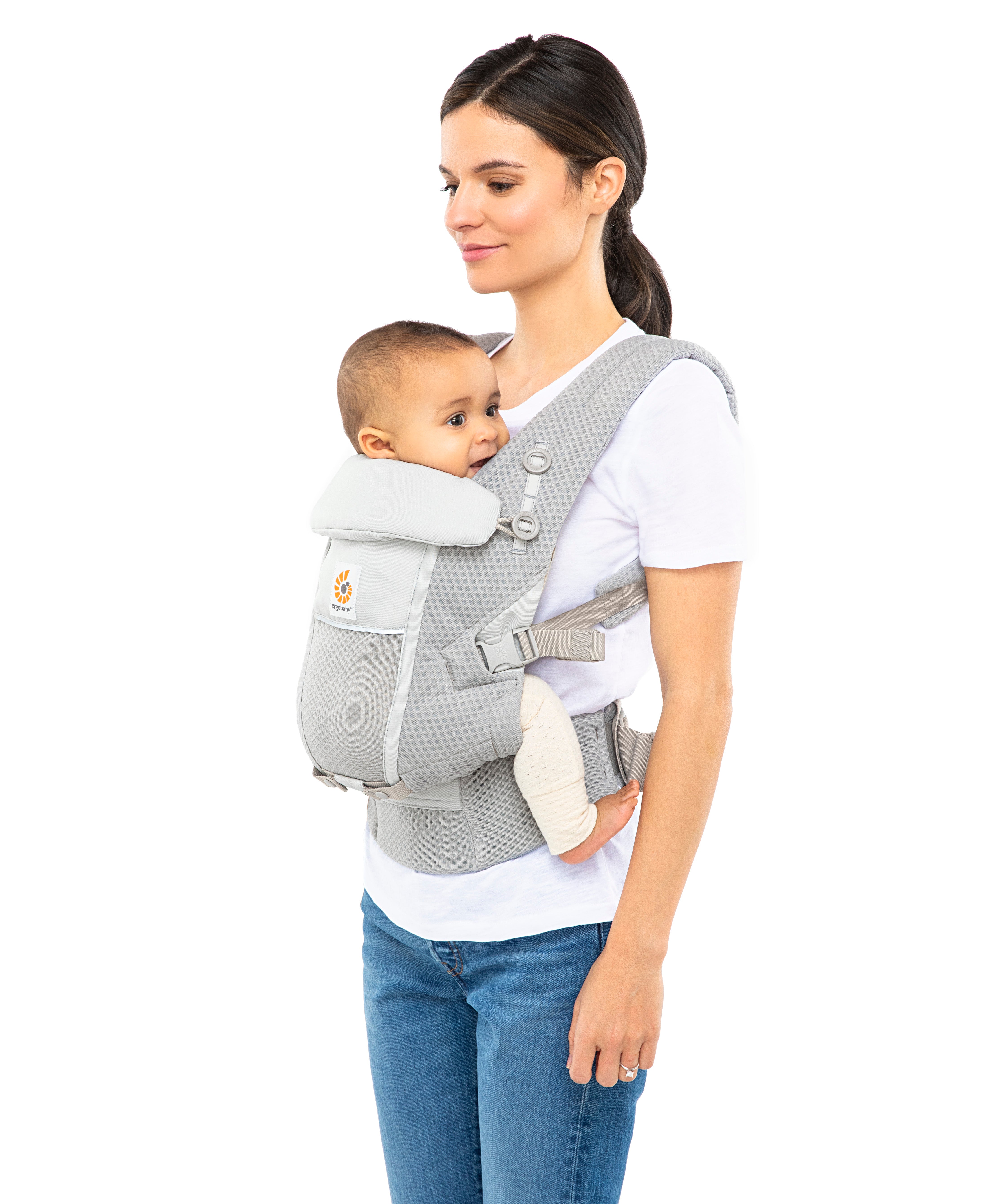 Woman with straight brown hair and a white t-shirt wearing her baby in the Ergobaby Adapt  SoftFlex™ Mesh Baby Carrier in Pearl Grey. Front view, white background. 