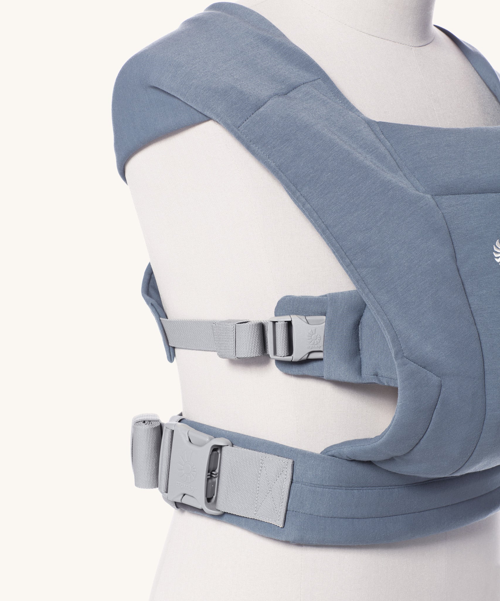 Close up of the buckles on the Ergobaby Embrace Soft Knit Newborn Baby Carrier in Oxford Blue. Side view on a mannequin.