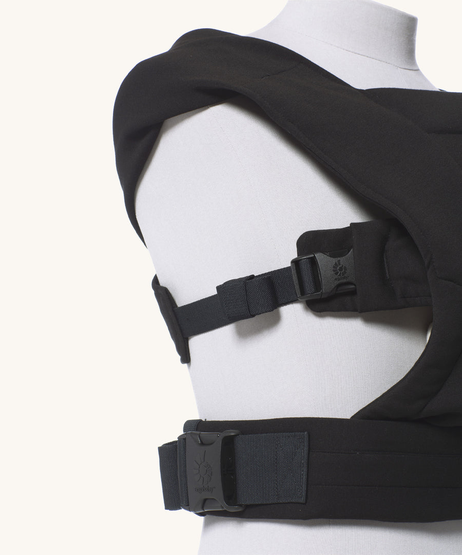 Close up of the buckles on the Ergobaby Embrace Soft Knit Newborn Baby Carrier in Pure Black. Side view on a mannequin.