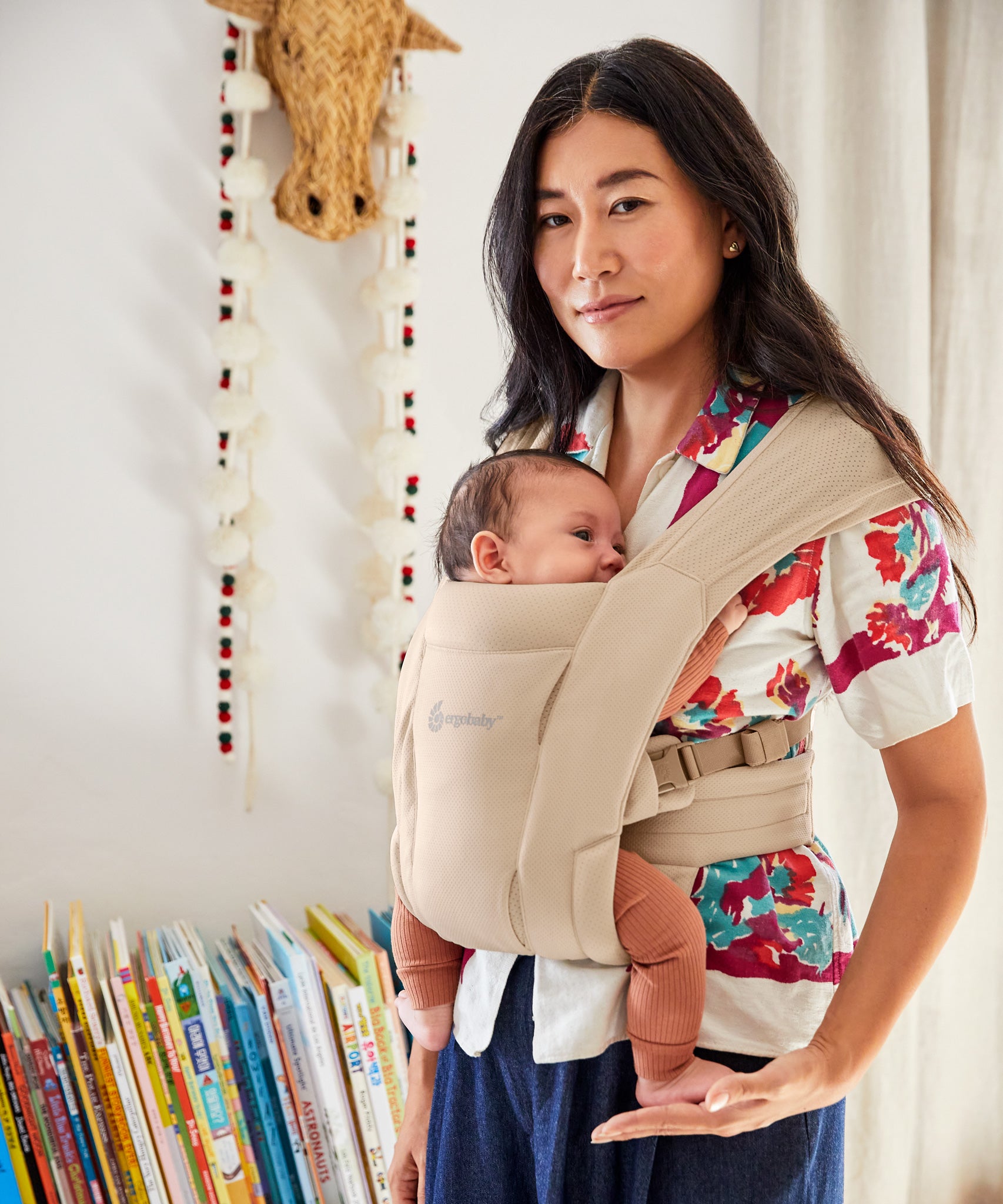 A woman babywearing using the Ergobaby Embrace Soft Air Mesh Newborn Baby Carrier in cream.