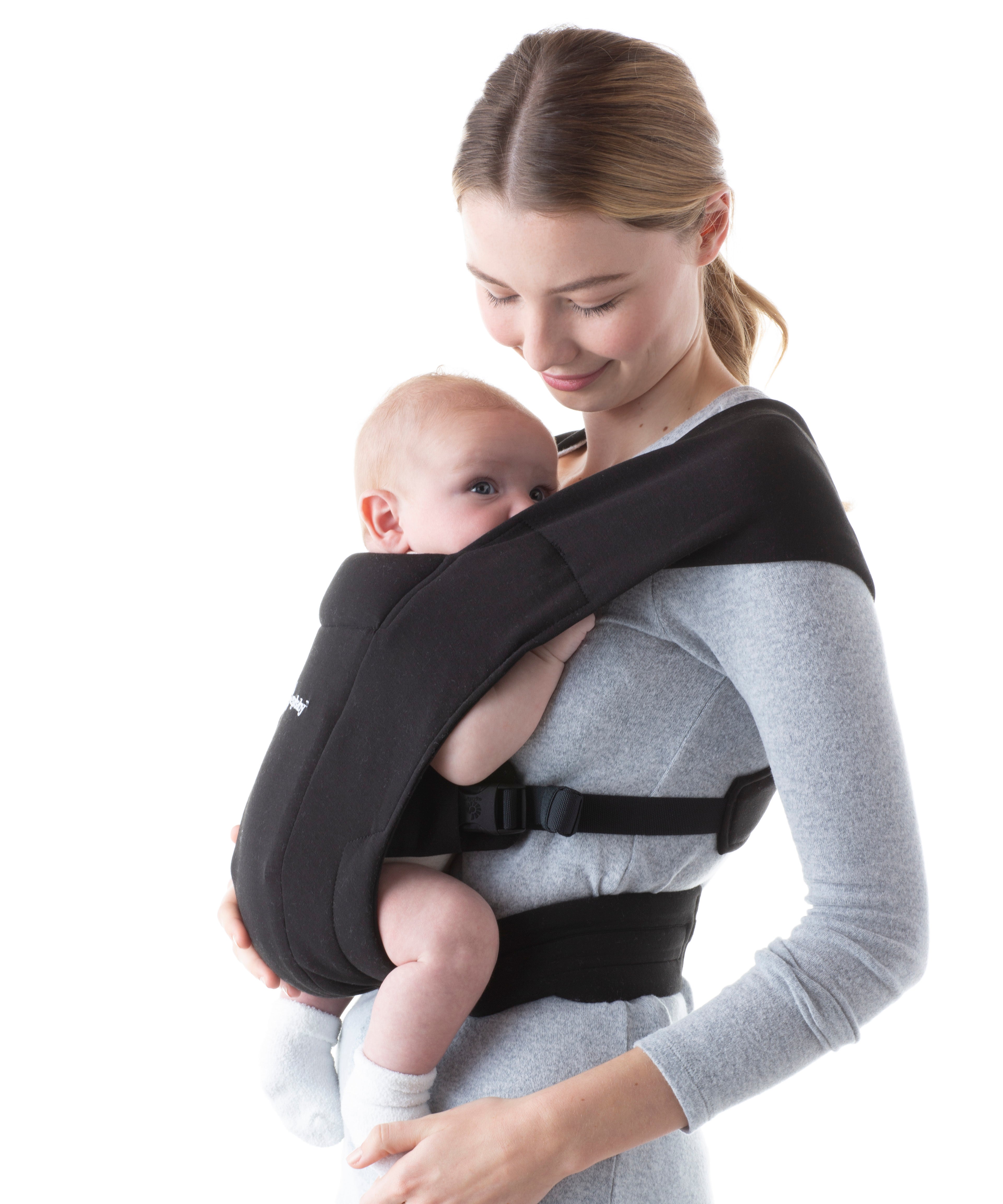 Woman wearing a grey top and her baby on her front in the Ergobaby Embrace Soft Knit Newborn Baby Carrier in Pure Black. Side view white background.