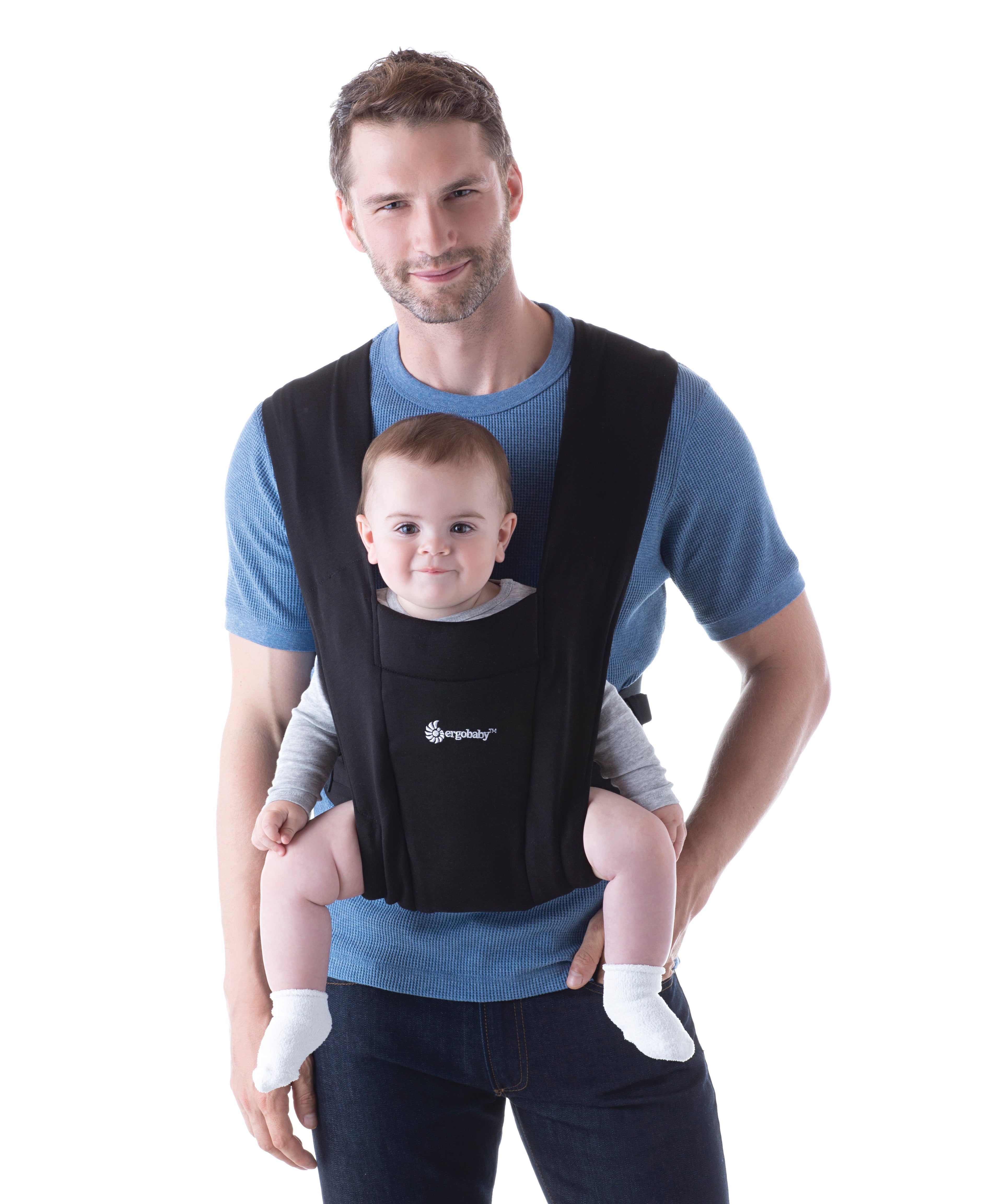 Man wearing a blue top and his baby on his front facing outwards in the Ergobaby Embrace Soft Knit Newborn Baby Carrier in Pure Black. Front view white background.