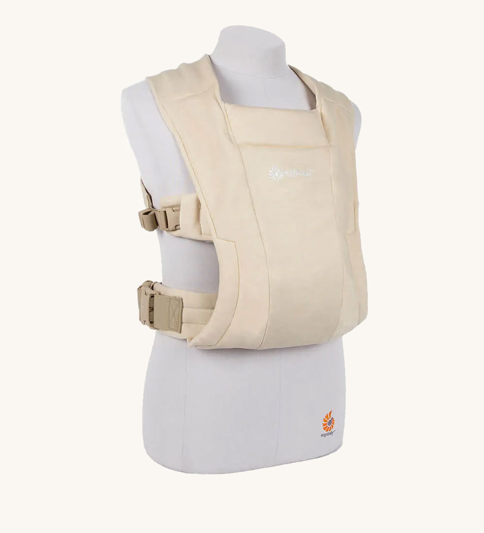 The Ergobaby Soft & Snug knit newborn baby carrier in a soft cream colour, from a side angle view.