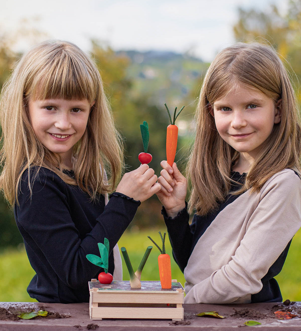 Two children playing with the Erzi Vegetable Patch Wooden Play Food Set. The child on the left is holding the red radish