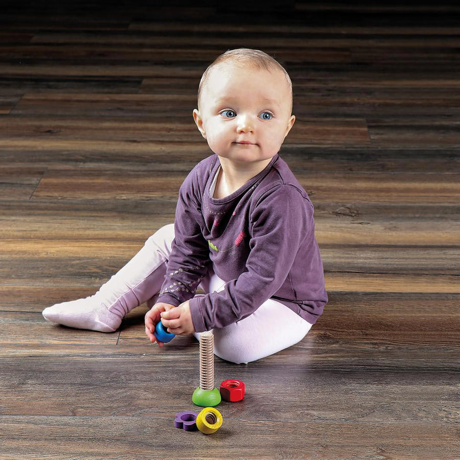 Toddler sat on a wooden floor playing with the Erzi eco-friendly rainbow screw turning learning game