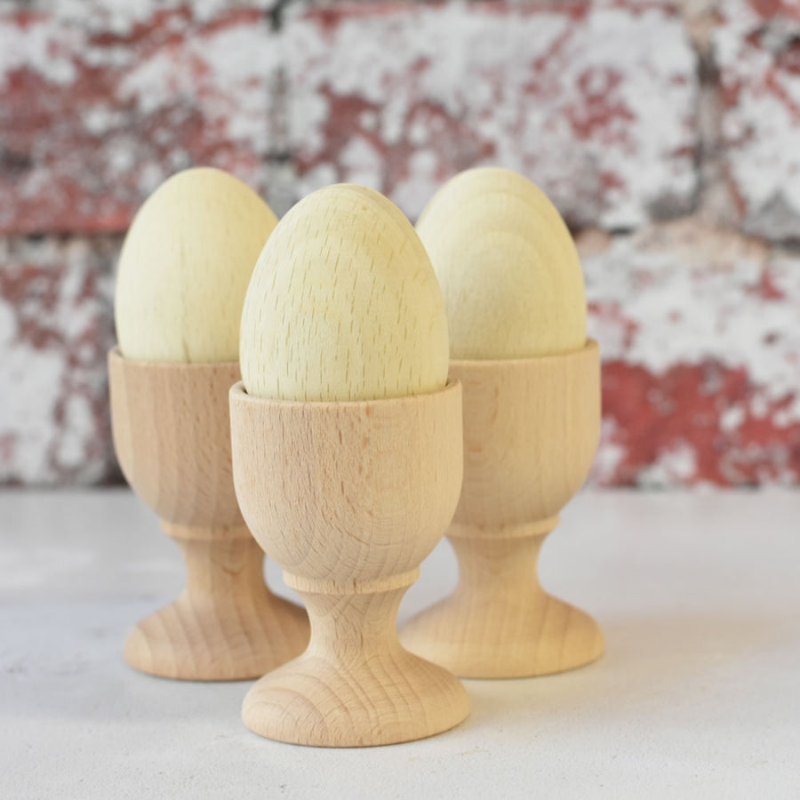 Three of the Erzi Six White Eggs Wooden Play Food in wooden egg cups