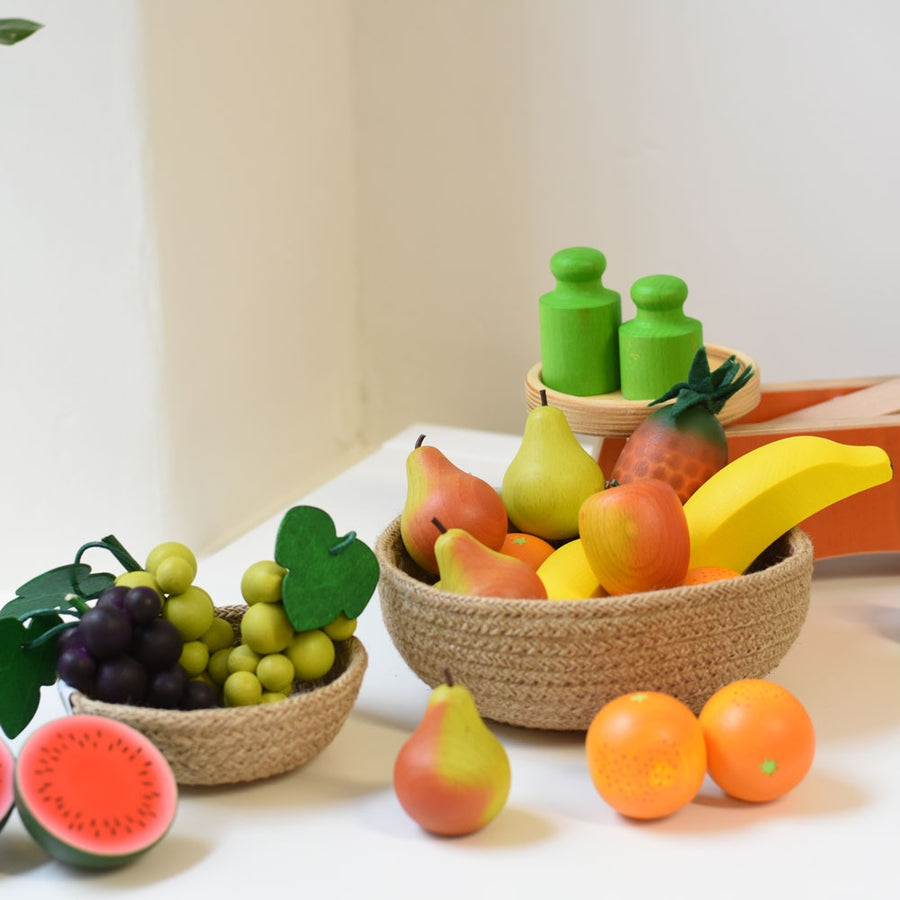 Erzi Orange Wooden Play Food in a woven bowl with other wooden toy fruits and a set of toy kitchen scales in the background.