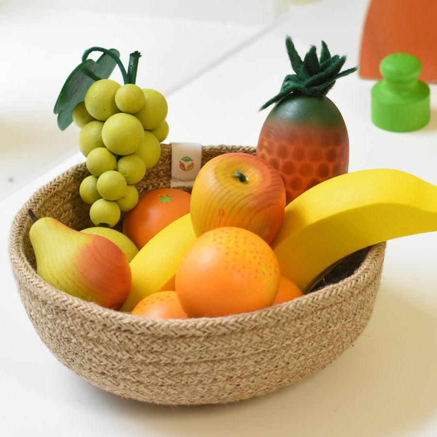 A Respiin natural woven basket displaying a selection of Erzi wooden toy fruit