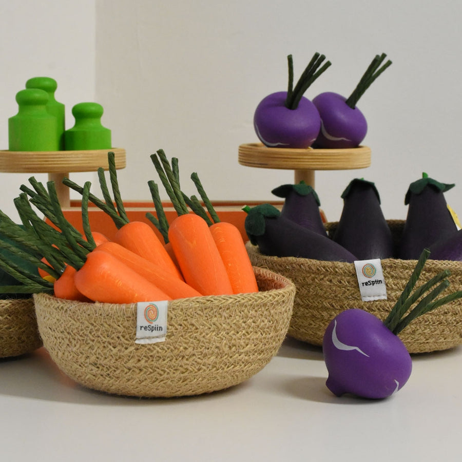 An Erzi Purple Turnip Wooden Play Food next to a natural woven bowl of play carrots