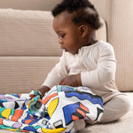 A baby with a A Etta Loves x Camille Walala XL Muslin Square in shapes design across their lap. 