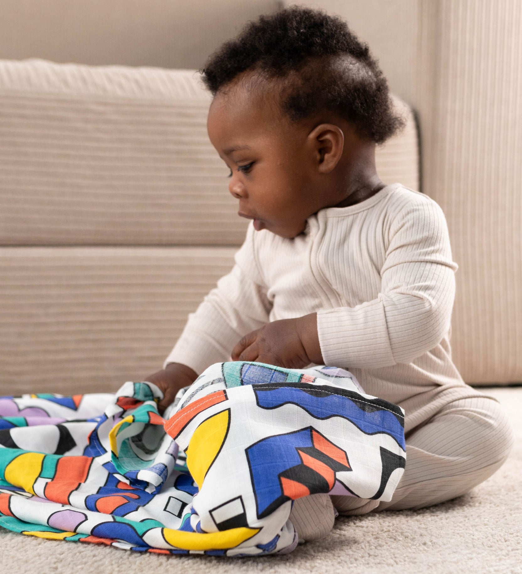 A baby with a A Etta Loves x Camille Walala XL Muslin Square in shapes design across their lap. 