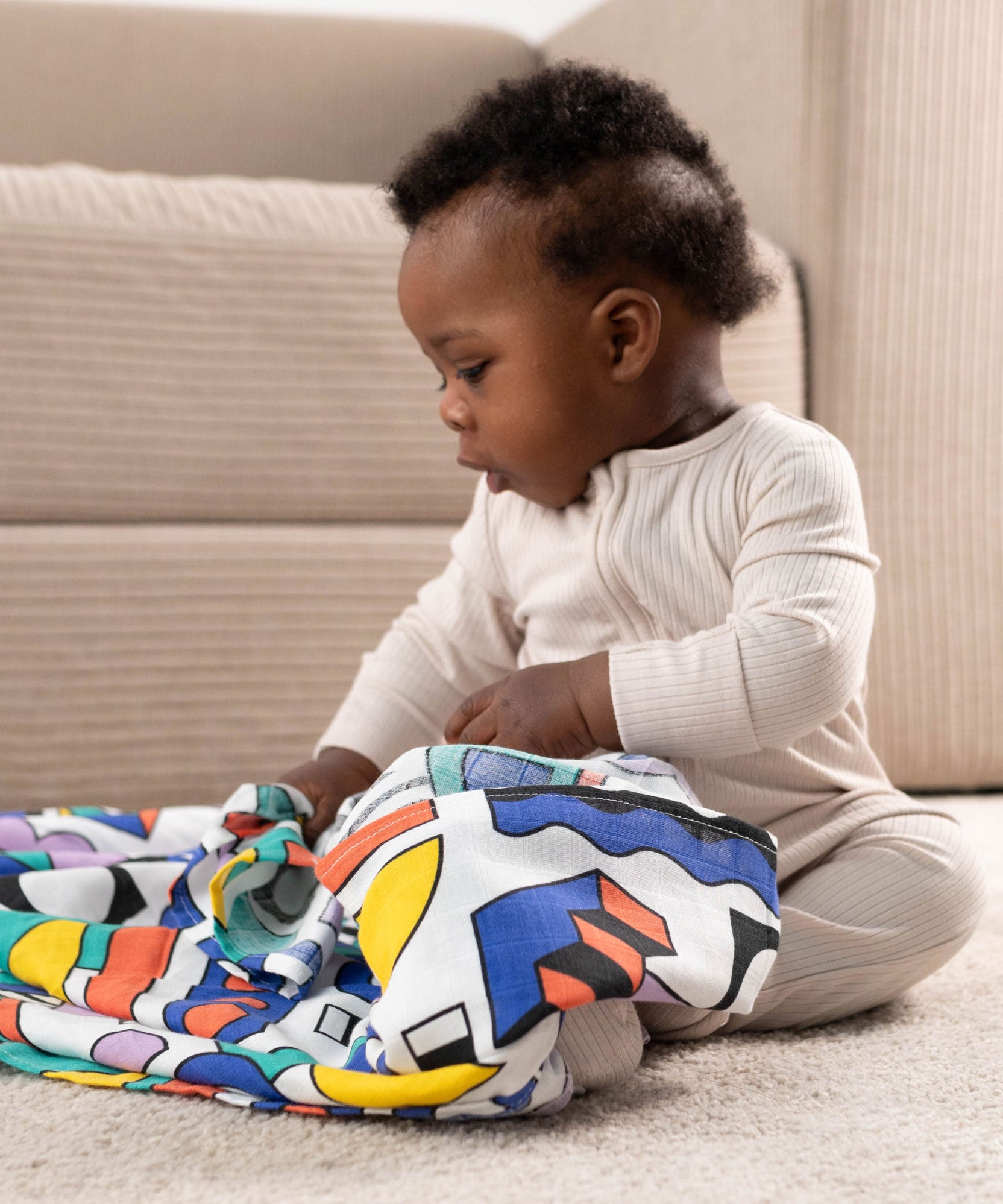 A baby with a A Etta Loves x Camille Walala XL Muslin Square in shapes design across their lap. 