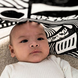 A baby laying underneath a Etta Loves x Camille Walala XL Muslin Square - Mono