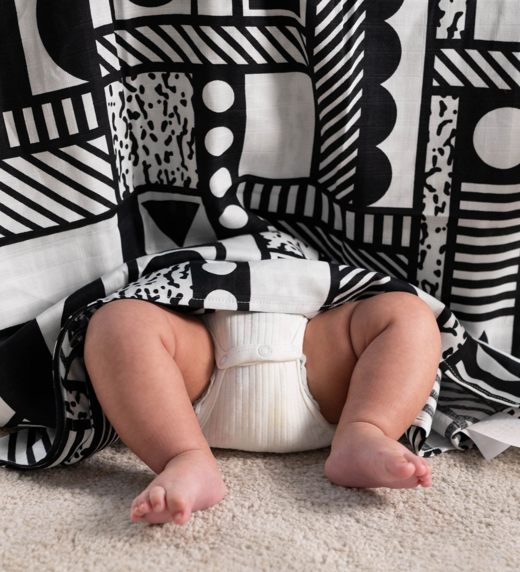 A Etta Loves x Camille Walala XL Muslin Square - Mono hung up, a baby's legs and feet can be seen popping out from underneath.