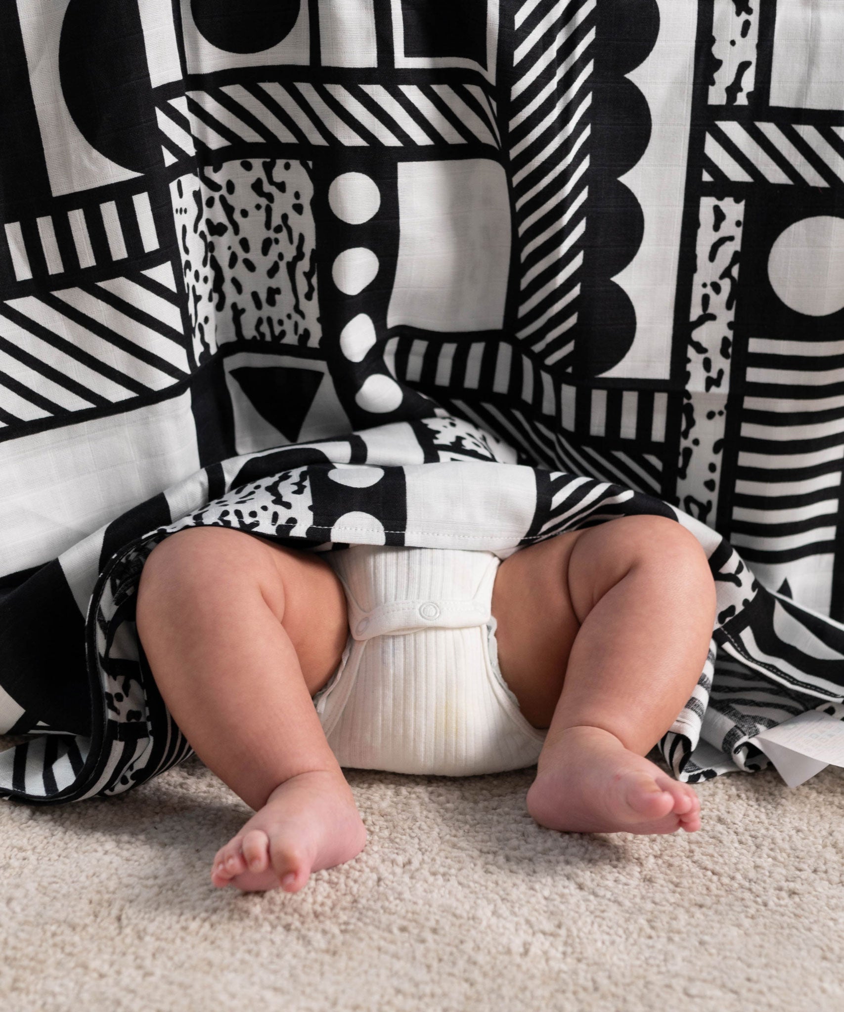 A Etta Loves x Camille Walala XL Muslin Square - Mono hung up, a baby's legs and feet can be seen popping out from underneath.