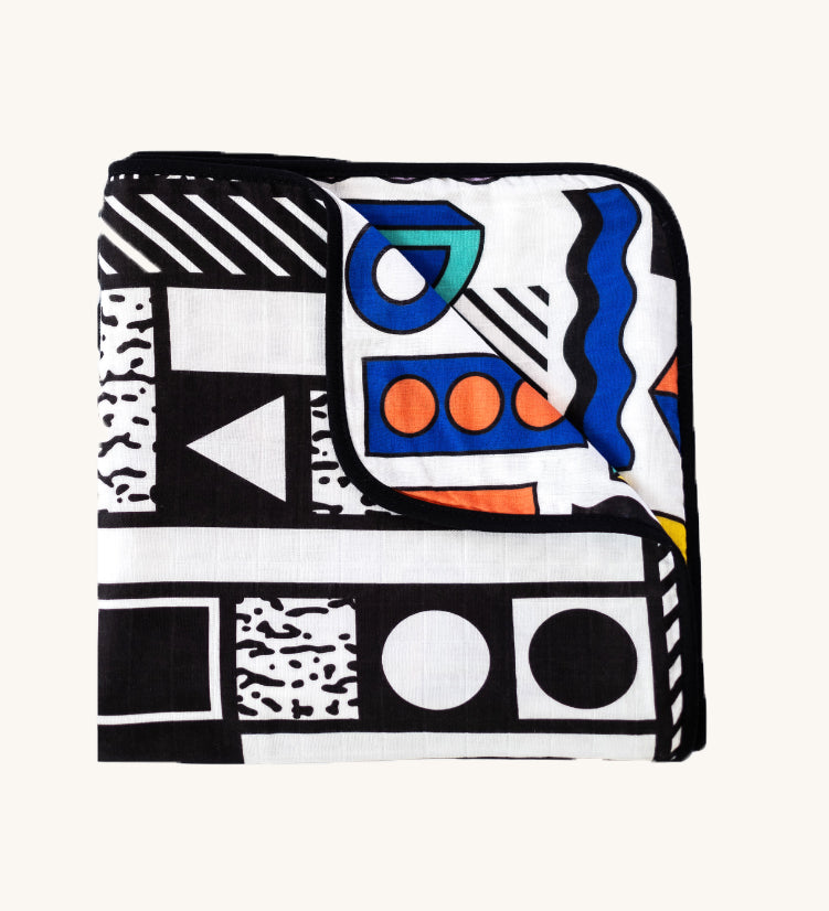 Etta Loves x Camille Walala Muslin Blanket folded into a square with one corner folded down showing the coloured side. 