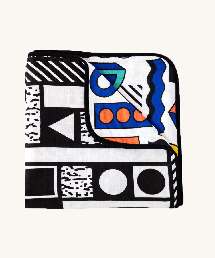 Etta Loves x Camille Walala Muslin Blanket folded into a square with one corner folded down showing the coloured side. 