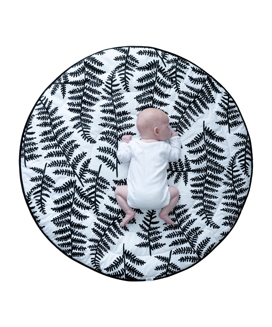 A toddler lying down on colourful Sycamore seed print on the Etta Loves Reversible Organic Cotton Baby Play Mat - Plant Print 