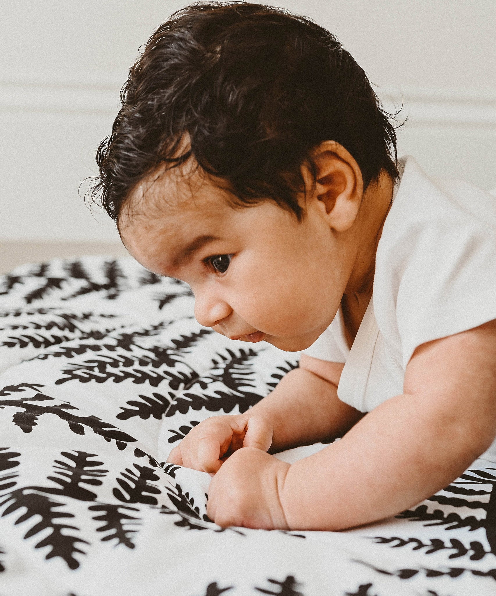 A baby lying down on the Etta Loves Reversible Organic Cotton Baby Play Mat - Plant Print with black and white Ferns